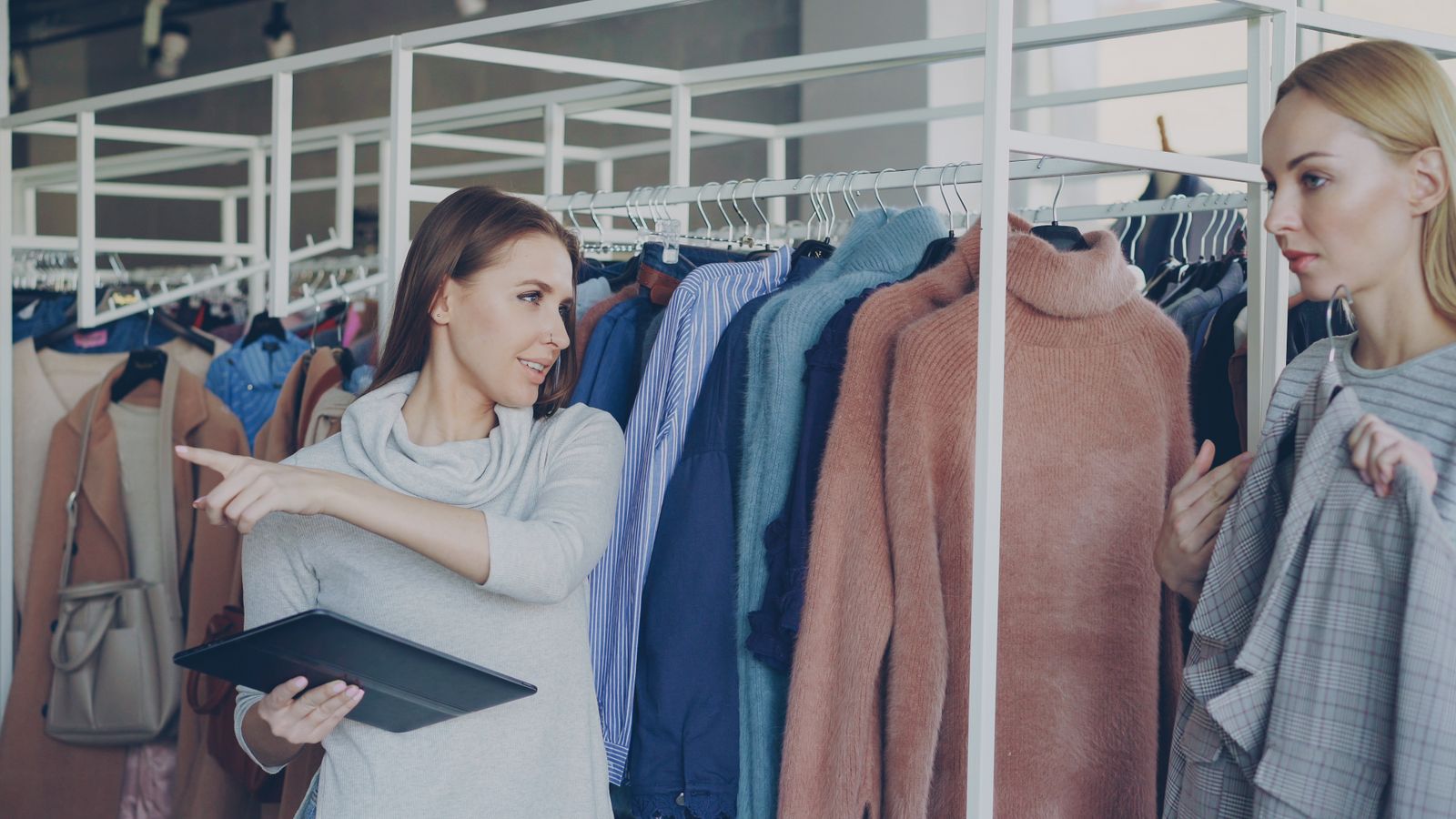Two women discussing clothing in a retail store, with a tablet in hand